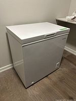 White Amana chest freezer showing front and top view in room corner.