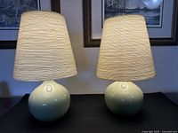 Front view of both lamps side by side on black surface against framed wall art background