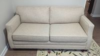 Front view of light taupe tweed textured fabric love seat sofa bed against wall, with seat and back cushions and two throw pillows.