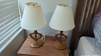 Full view of pair of teak mid-century modern bedside table lamps on wooden bedside table.