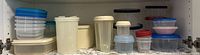 Shelf with assorted plastic storage containers in various shapes and sizes, including round, square, and rectangular, with blue, white, beige lids