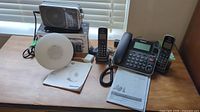 Photo showing Panasonic 2-in-1 corded/cordless phone, Panasonic RF-2400D radio in original box, Philips wake up light, and user manuals on a table.