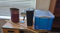 Photo showing all items including shredder, blue plastic file box, yard sticks, metal waste basket and desk lamp on wooden surface.