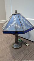 Full view of lamp showing the blue stained glass shade with milkweed seed pattern and metal base resembling a tree trunk.