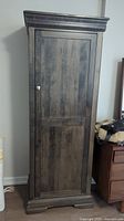 Tall wood look veneer cabinet with closed door showing dark wood grain finish and molding details.