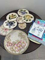 Image showing multiple vintage floral hot pads and pot holders on a dark round table along with a lavender sachet packet