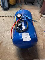 Blue cylindrical 10 gallon air tank laying on side with pressure gauge, air hose, and nozzle attached, placed on workshop floor.