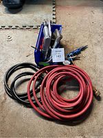 Photo of assorted air tools including air sandblaster, air drill, two coiled air hoses (red and black), and a blue air hose fitting. Items stored in a blue metal container.