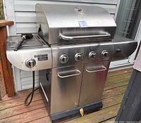 Front view showing stainless steel grill with four burner control knobs and one side burner control knob, hood with temperature gauge