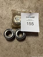 Four NTN tapered roller bearings, three unpackaged and one in sealed plastic bag, displayed on concrete floor with MaxSold number card 155.