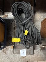 Photo showing heavy-duty black extension cord coiled on top of a dark plastic toolbox with yellow plug visible, placed on a concrete floor.