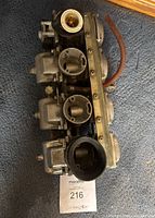 Side angle view of the Mikuni Kogyo Co. triple motorcycle carburetor on carpet, showing the body, fuel bowls and throttle valves.