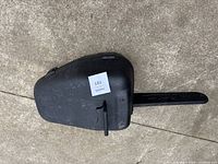 Closed black hard plastic carrying case for chainsaw, showing the handle and latch.