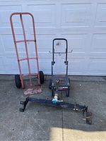 Overall view of the two-wheel dolly, Craftsman pressure washer dolly, and vehicle hitch lying side by side on a concrete surface in front of a garage door.