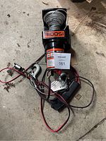 Top view of the electric winch showing the coiled metal cable, hooks, wiring, and label.