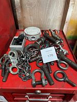 Various metal eye bolts, anchor shackles, chains, a round junction box on a red surface