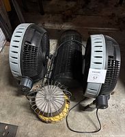 Photo shows two round fans, one black bug zapper in the middle, and a catalytic heater with metal cage and yellow base on the floor.