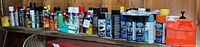 Wide angle view of a long row of various garage chemical spray cans and bottles on a wooden shelf.