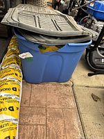 Rubbermaid rubber floor mats stacked on top of a blue plastic bin with yellow coiled tubing beside them.
