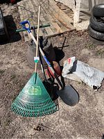 Photo of rake, shovel, pots, and bags placed on the ground showing contents of gardening lot.