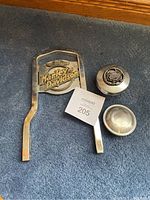 Two gas caps and one Harley-Davidson sissy bar placed on carpet.