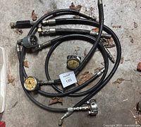 Multiple pressure gauges connected to hoses laid on concrete floor, showing their size and condition.