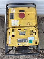 Top view of yellow fuel tank and control panel covers with labels attached, surface dirt present.