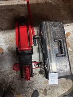 Top view of red hydraulic floor jack and metal tool box side by side on concrete floor