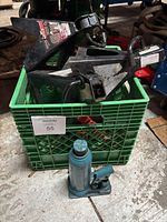 Four black axle stands with red locks in a green crate, and a blue hydraulic bottle jack placed in front on the floor.
