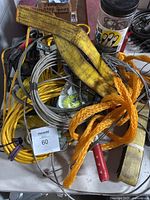 Mixed hardware items including yellow straps, metal cables, orange braided ropes, and a battery charger in a container.