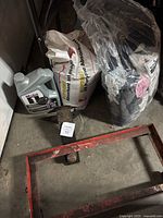Photo of vehicle jack, metal cart frame, motor oil container, absorbent bag, and cotton wipes bag.