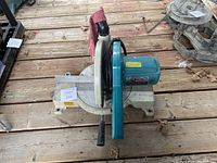 Angled view of Makita LS1030 miter saw showing blade guard, handle, and motor housing on wooden floor.
