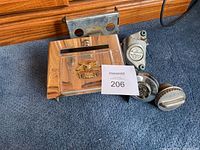 Group photo of Harley-Davidson motorcycle parts including chrome battery box cover with emblem, brake caliper, bracket and two round gas caps.