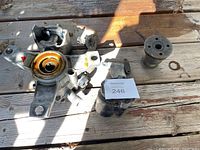 Photo showing several metal motorcycle parts including a front brake caliper, clutch ball and ramp assembly, a piston, and mounting brackets on a wooden surface.