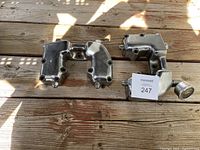 Two polished metal motorcycle parts: rocker box and rocker box oil pressure gauge with tubular connection, placed on wooden surface.