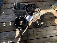 Overview of clutch assembly, transmission parts, sprockets, and chain, laid out on a wooden surface under partial sunlight.