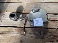 Motorcycle parts including air filter, hand control lever, sprocket cover, and small metal parts displayed on wooden surface in natural light.