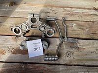 Photo showing motorcycle triple tree, handlebar clamp, shifter pedal and shift lever laid on wooden surface.