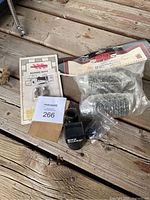 Photo showing bungee nuts, chrome cap replacement pegs in bubble wrap and packaging, metal clamp, cables, and Bike Guard alarm device all placed on wooden surface.