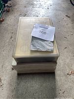 Stack of three plastic containers on concrete floor, one container is translucent showing contents inside.