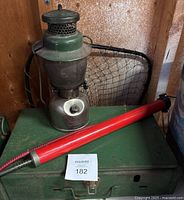 Overall view of green outdoor lantern, red tire pump, fishing net behind and green outdoor stove below