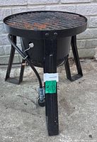 Front angled view of portable outdoor gas grill showing round grill grate, black metal construction, and attached gas hose.