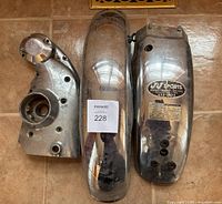 Wide top-down view of all three parts: engine cam cover on the left, rear fender in the center with badge plate, and front fender on the right.