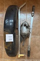 Black front fender, gearbox outer cover, highway bar, and metal handle laid on tiled floor.