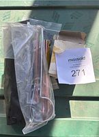 Photo of metal wrenches, pivot shaft, and other hardware parts in a plastic bag on a green surface