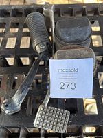 Photo showing the motorcycle brake pedal, footpeg, and two pistons laid out on a metal grid surface.