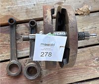 Crankshaft and two connecting rods laid on wooden surface with auction tag showing lot number 278.
