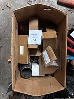 Box containing multiple small cardboard boxes and a metal pipe piece, showing various packaged and unpackaged parts.