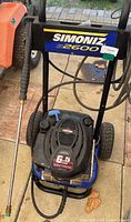 Pressure washer showing front and wheels with Simoniz S2600 label and orange spray wand.