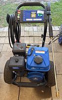 Front view of pressure washer mounted on black steel frame with pneumatic wheels and blue engine tank.